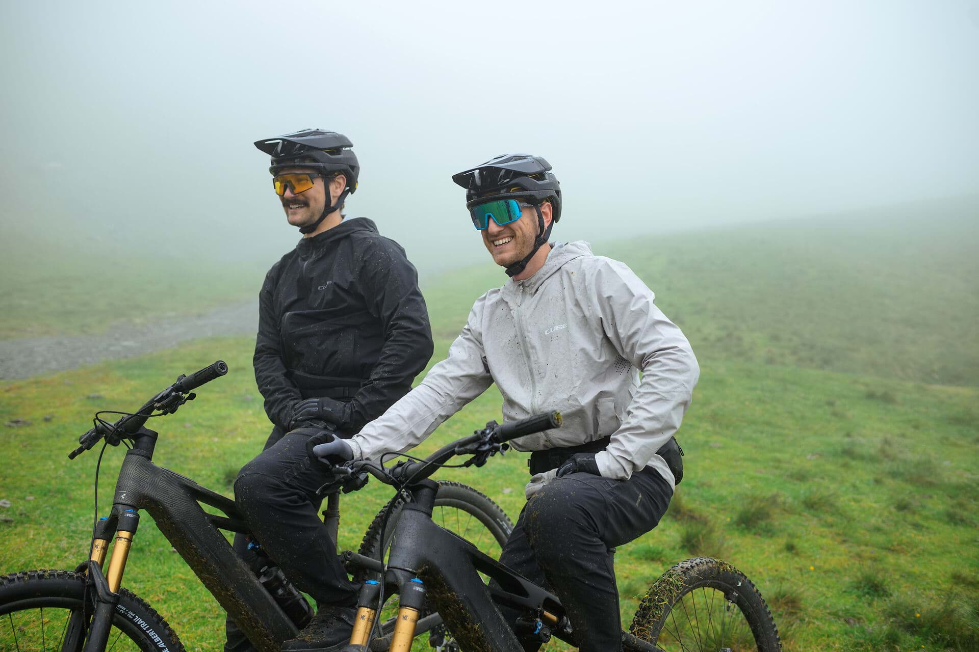 Zwei Radfahrende auf einer Almwiese im Nebel